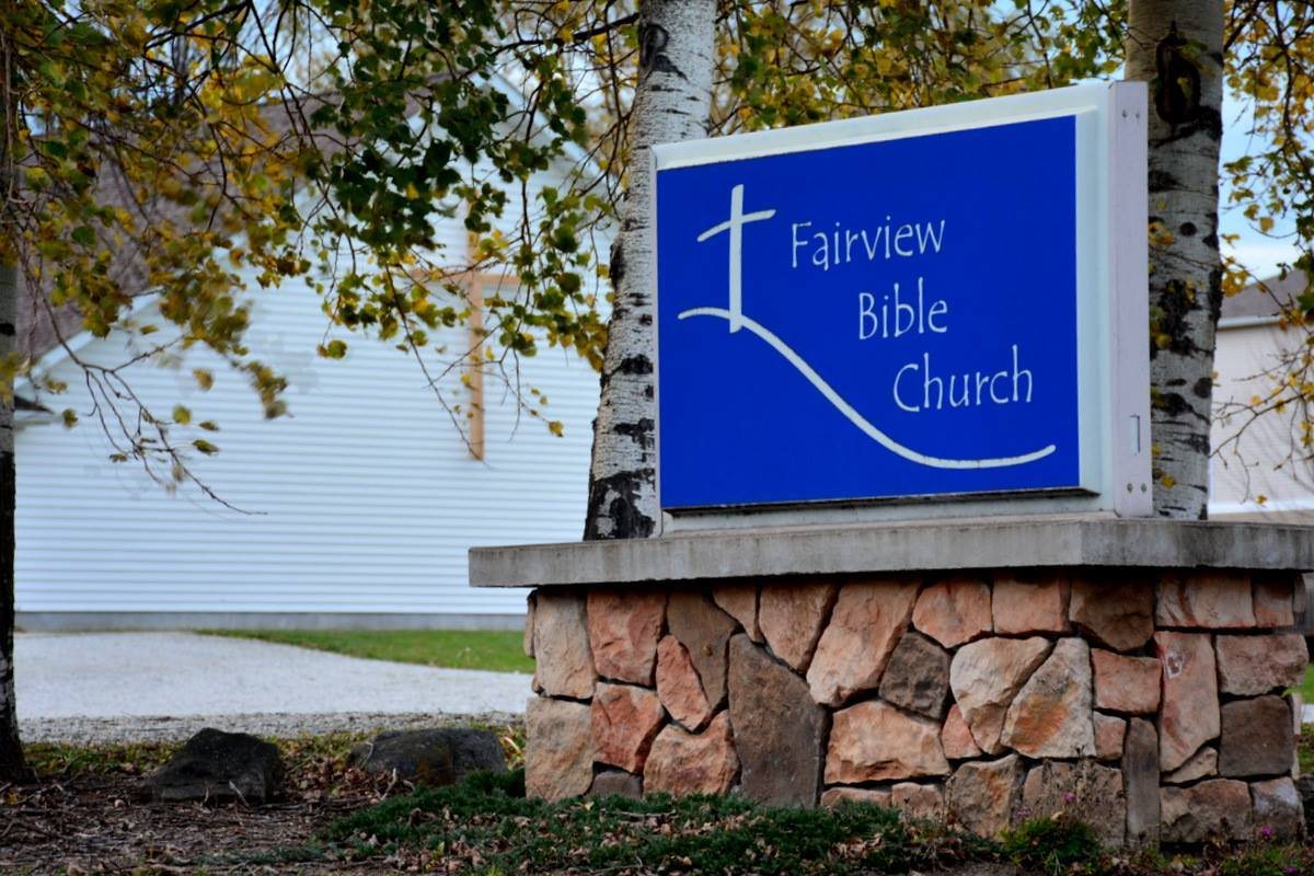 The church sign and the white clapboard building behind it
